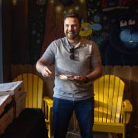 Man in grey shirt and jeans smiling as he grabs pizza